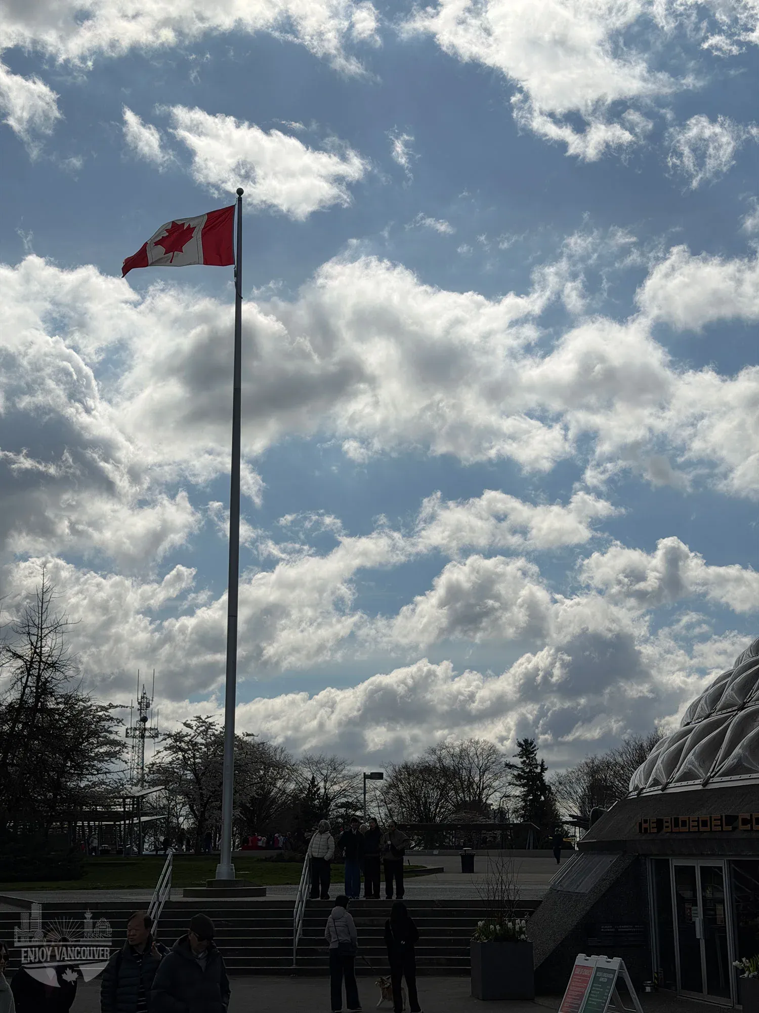 Canadian flag flying at Queen Elizabeth Park with Bloedel Conservatory dome and visitors in Vancouver